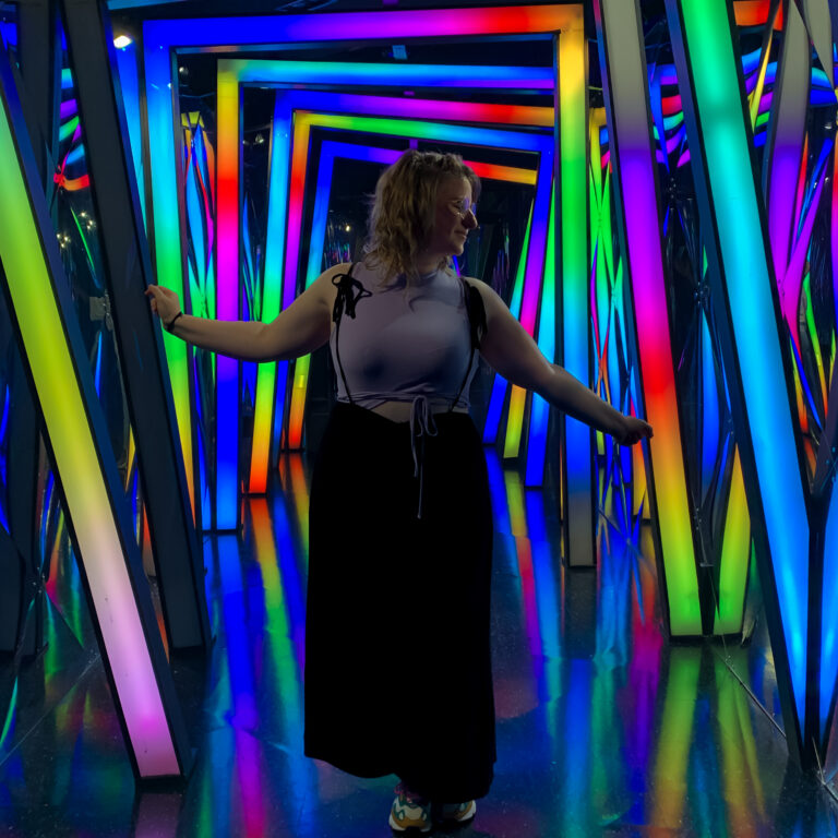Wendy in between frames that gives off a neon light. She has her arms spread out and looks to the side.