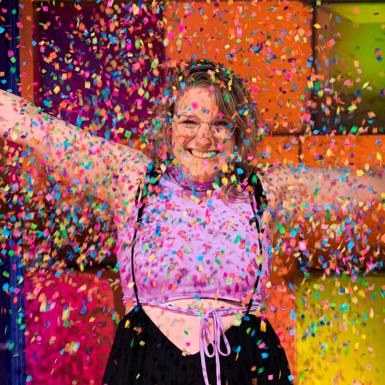 Wendy smiling at the camera, her arms spread out, while colorful confetti flies all around her.