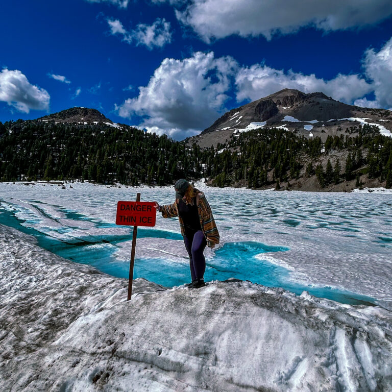 Wendy in front of a frozen lakee, surrounded by snow, with a warning sign saying 'danger thin ice'