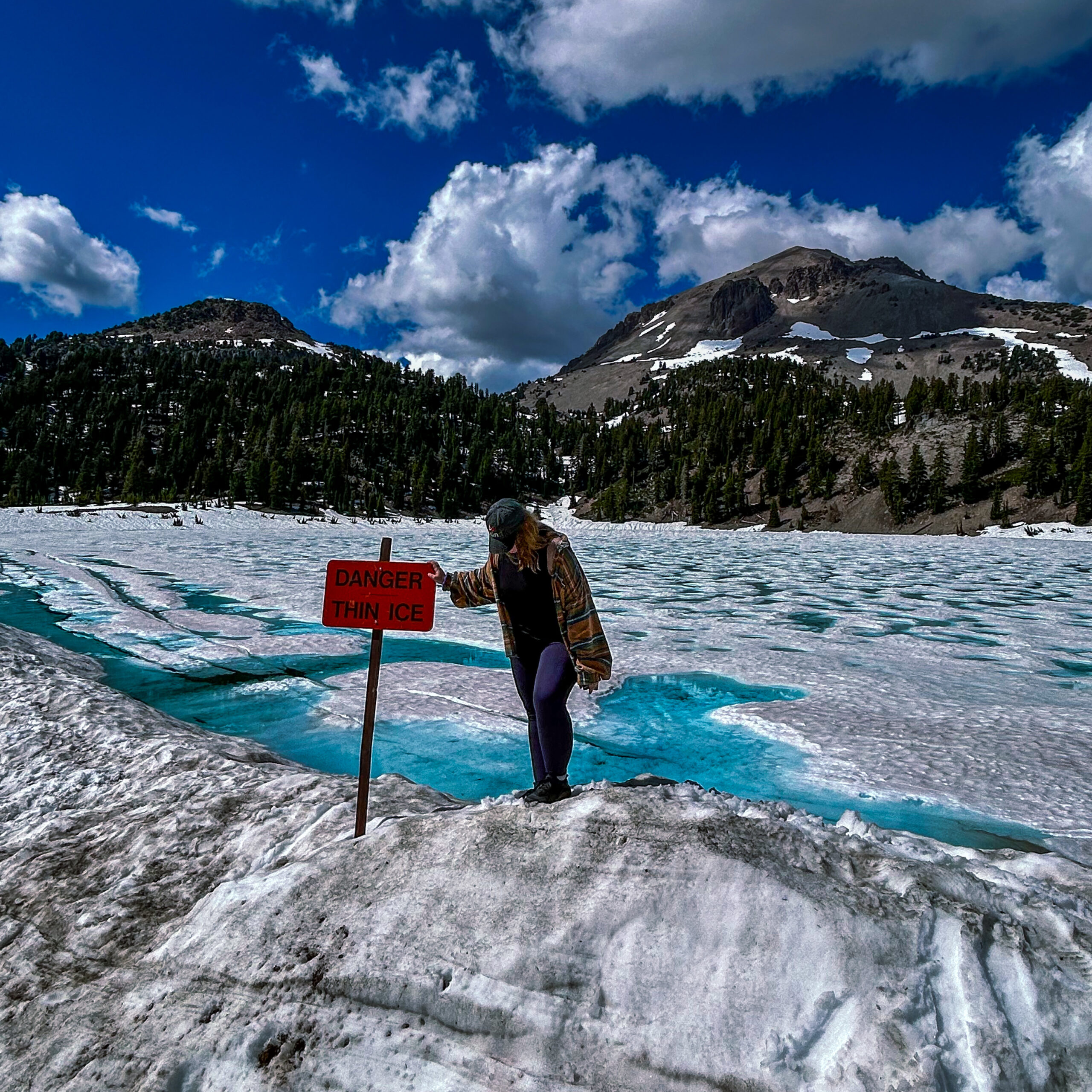 Wendy in front of a frozen lakee, surrounded by snow, with a warning sign saying 'danger thin ice'