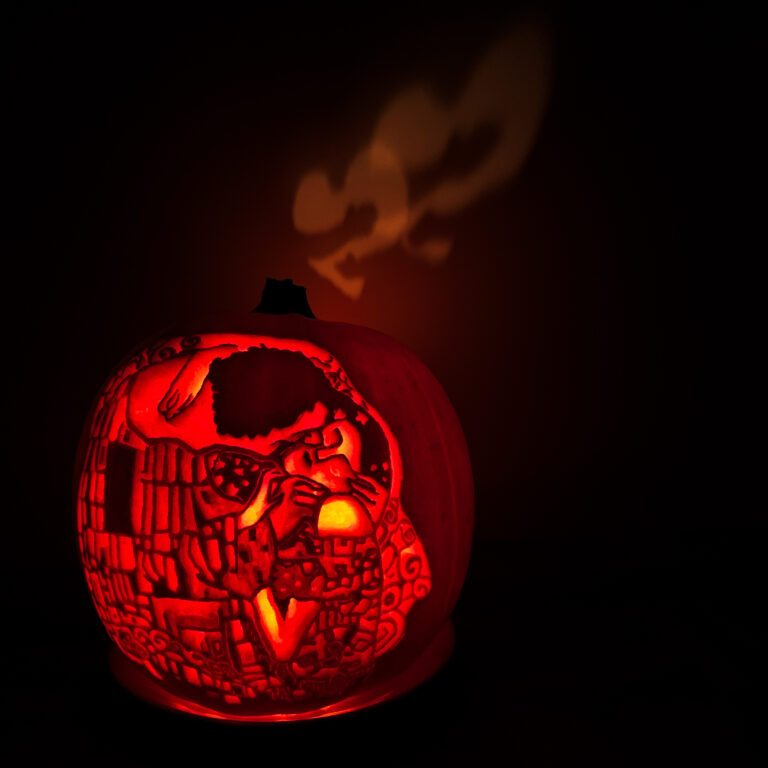 a pumpkin carved with the image of Klimt's painting 'The Kiss' with in the back a heart projected on the wall